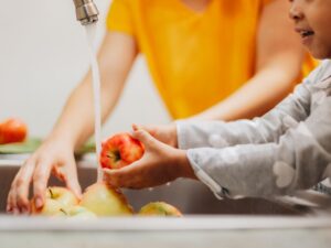 Child and adult washing fruit together, promoting healthy habits for kids.