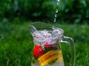 A clear pitcher filled with water, fresh strawberries, and lemon slices outdoors, representing healthy drinks for kids.