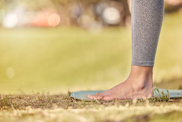 Close-up of a bare foot stepping onto a yoga mat on grass in an outdoor park setting.