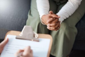 Close-up of a therapist's hands clasped together while taking notes on a clipboard during a counseling session.