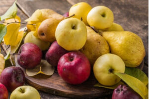 Red and yellow apples with golden pears on a rustic wooden board.